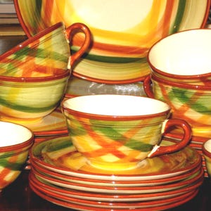Könnte beinhalten: Ein Set aus Keramikgeschirr mit einem farbenfrohen Karomuster. Das Set umfasst Tassen, Untertassen und Teller in Orange, Grün und Gelb. Die Tassen haben Henkel und sind gestapelt. Die Teller sind in einem Stapel angeordnet.