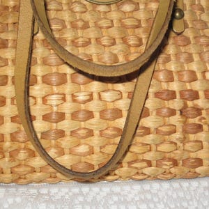 K&ouml;nnte beinhalten: Eine geflochtene Strohtasche mit Lederriemen. Die Tasche ist hellbraun und hat ein geflochtenes Muster.