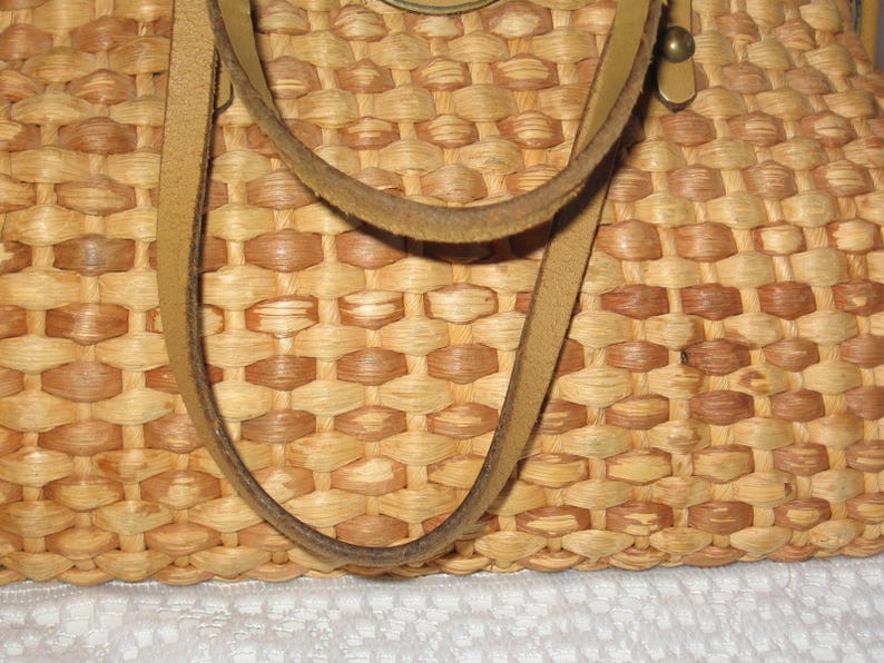 K&ouml;nnte beinhalten: Eine geflochtene Strohtasche mit Lederriemen. Die Tasche ist hellbraun und hat ein geflochtenes Muster.
