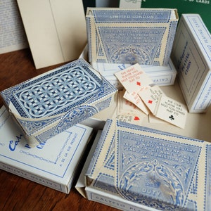 May include: A close-up of a set of Calypso playing cards in their original boxes. The boxes are blue and white with intricate designs and the text "Calypso Playing Cards" and "De La Rue Product".