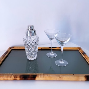 Op de afbeelding: Een cocktailset met een kristallen glazen shaker met een zilveren deksel, twee martiniglazen en een bamboe dienblad met een donkergrijze oppervlakte. De dienblad heeft een rechthoekige vorm en is gemaakt van bamboe.