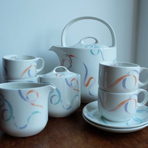 May include: A white tea set with a colorful abstract design. The set includes a teapot, creamer, sugar bowl, and two cups and saucers.