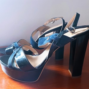 Puede incluir: Un par de sandalias de plataforma negras con una tira de ante y un tacón alto.