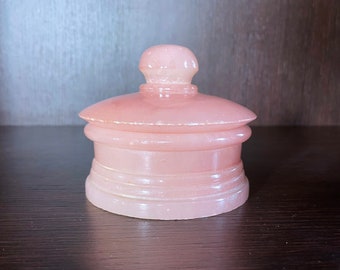 May include: A pink alabaster trinket box with a rounded lid and a decorative band around the base.