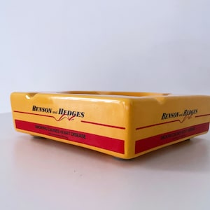 May include: Yellow ceramic ashtray with the Benson & Hedges logo and the text "Smoking causes heart disease".