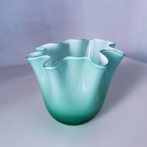 Könnte beinhalten: Eine Glasschale mit einem gerüschten, gewellten Rand und einem Farbverlauf, der von einem tiefen, satten Grün an der Basis zu einem helleren, blassen Mintgrün und Weiß am oberen Rand übergeht und einen glatten, durchscheinenden Effekt erzeugt.