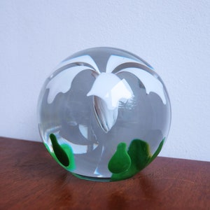 May include: A clear glass paperweight with a white flower design and green accents.