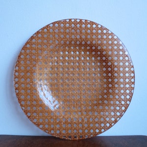 May include: A round, clear glass plate with a woven wicker pattern. The plate is brown and has a glossy finish.