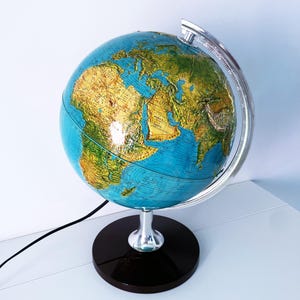 May include: A vintage globe with a blue ocean and detailed landmasses in shades of green and yellow. The globe is mounted on a silver meridian and a black base. A black power cord extends from the base.