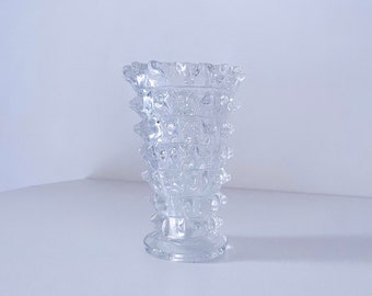 May include: A clear glass vase with a textured, geometric design. The vase has a wide mouth and a narrow base.
