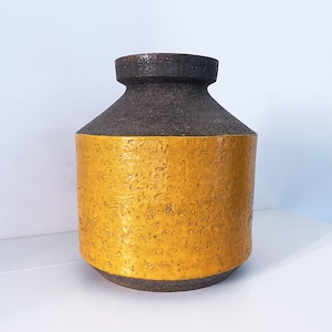 May include: A textured, mid-century modern vase with a cylindrical body and a dark brown top. The lower portion of the vase is a vibrant yellow-gold colour. The vase is likely made of ceramic or stoneware.