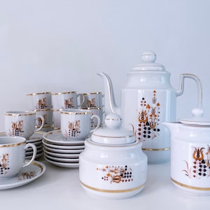 Puede incluir: Un juego de té de porcelana blanca con ribetes dorados y un patrón floral. El juego incluye una tetera, una jarra de crema, un azucarero y seis tazas y platillos.