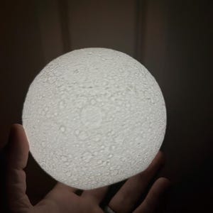 May include: A white moon-shaped night light with a textured surface, resembling the moon's craters.