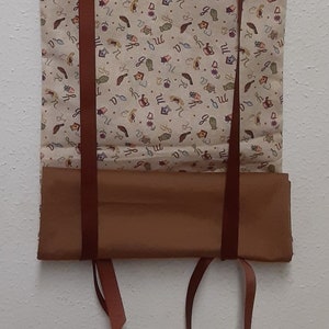 May include: A brown fabric valance with a white fabric lining. The valance has a pattern of small, colorful images and text. The valance has brown straps on the sides.