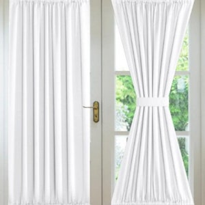 May include: A pair of white sheer curtains with a ruffled top and bottom, hanging on a double French door. The curtains are tied back with a white ribbon.