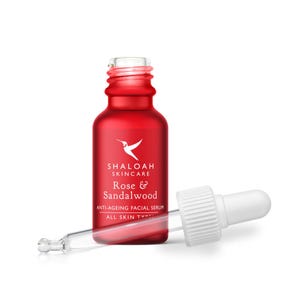 Peut inclure: Un flacon en verre rouge de sérum facial anti-âge Shaloah Skincare Rose & Sandalwood pour tous types de peau. Le flacon présente un logo colibri blanc et du texte, accompagné d'un bouchon compte-gouttes blanc posé horizontalement devant.