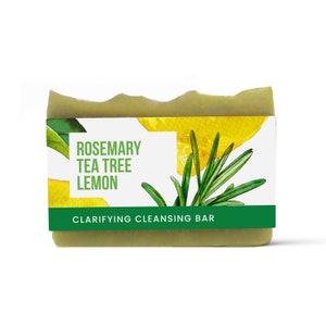 Peut inclure: Un savon en barre vert avec une étiquette blanche qui indique "Rosemary Tea Tree Lemon Clarifying Cleansing Bar". L'étiquette présente également une illustration aquarelle d'une tranche de citron et de brins de romarin.