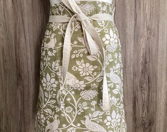 Green floral half apron with two pockets. Birds and hares cotton fabric. Plus size, wide half apron with long straps. Heathland Moss.