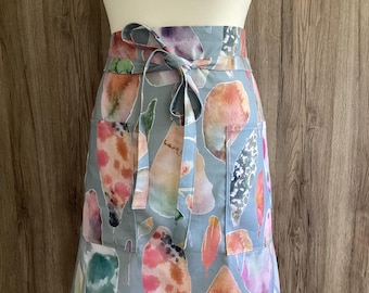 Wide half apron with long straps and two pockets. Plus size apron in cotton fabric. Blue/grey with large leaves