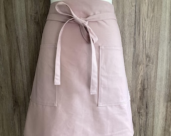 Pale pink wide half apron with two pockets and long straps in thick, soft cotton fabric.