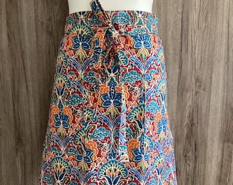 Wide half apron with two pockets and long straps in blue, red, green and orange cotton fabric. Iliv Rhapsody Ruby. Floral apron.
