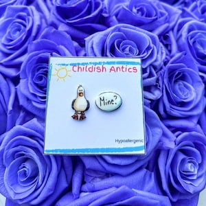 May include: A pair of hypoallergenic earrings featuring a cartoon seagull and a speech bubble that says "Mine?" The earrings are displayed on a white card with the text "Childish Antics" and "Hypoallergenic".