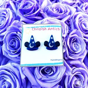 Op de afbeelding: Een paar blauwe en zilveren Mickey Mouse-oren met een ster- en maanontwerp. De oorbellen zijn hypoallergeen en worden gepresenteerd op een witte kaart met de tekst "Childish Antics".