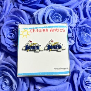 May include: A pair of hypoallergenic earrings featuring a white cloud with a blue "Soarin'" text and a yellow sun. The earrings are displayed on a white card with the text "Childish Antics" and "Hypoallergenic".