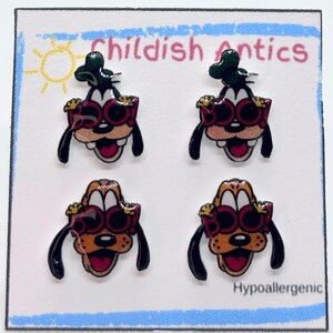 May include: Four stud earrings arranged on a white display card labeled Childish Antics and Hypoallergenic. The earrings feature cartoon dog faces wearing red glasses with the word BOO printed on the lenses. Two are black and white, two are tan.
