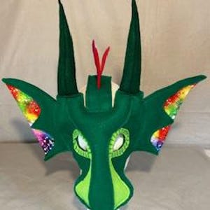 May include: Green felt dragon mask with rainbow iridescent accents on the ears and a red felt crest. The mask has green felt eyes and white felt teeth.