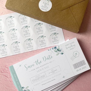 May include: Save the date cards with a light blue and green watercolour design. The cards are shaped like airline boarding passes with the text "Save the Date" and "First Class Boarding Pass". The date is 08.09.2023.