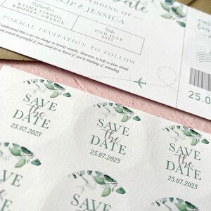 May include: Save the Date stickers with a watercolour eucalyptus design. The stickers are round and feature the text "Save the Date" with the date "25.07.2023".