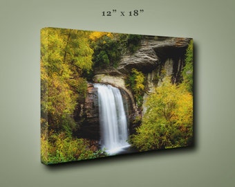 May include: A canvas print of a waterfall cascading down a rocky cliff face, surrounded by lush green trees with hints of yellow autumn foliage. The print measures 12 inches by 18 inches.