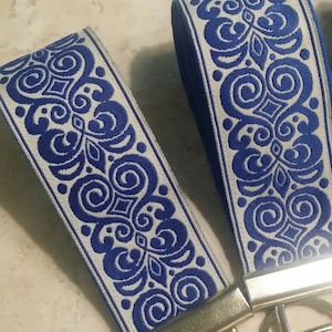 May include: Two white and blue patterned keychains with silver key rings. The pattern is a repeating design of swirls and leaves.