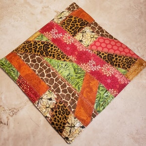 May include: A patchwork fabric hot pad with a variety of patterns, including leopard print, floral, and paisley. The hot pad is made of different colors, including brown, orange, green, pink, and red.
