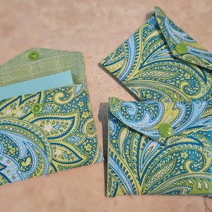 May include: Three green and blue paisley patterned fabric pouches with green buttons. The pouches have a flap that folds over and closes with a button.