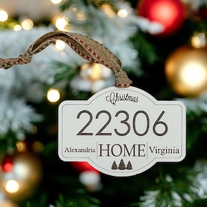 May include: A white Christmas ornament with the text "Christmas" and the numbers "22306". Below the numbers are the words "Alexandria HOME Virginia" and three small trees. The ornament has a burlap ribbon.