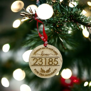 以下が含まれることがあります： 「There's no place like home」の文字と数字「23185」が入った丸い木製のクリスマスオーナメント。赤いリボンが付いていて、吊り下げられます。「FOR THE HOLIDAYS」の文字も含まれています。クリスマスデコレーション。