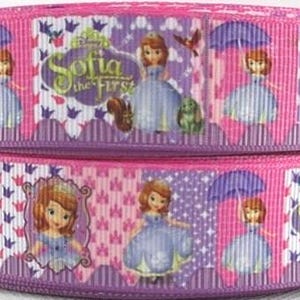 May include: Two stacked rolls of pink ribbon featuring the Disney character Sofia the First. The ribbon has a repeating pattern of Sofia in a blue dress, purple umbrellas, and the show's logo. The edges are a darker purple.