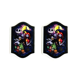Może przedstawiać: Dwa pasujące, dekoracyjne elementy w kształcie tarczy z kolorową ilustracją Jacka Skellingtona i Sally z Miasteczka Halloween. Grafika zawiera pełnię księżyca i r&oacute;żne postacie.