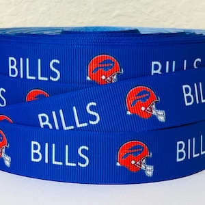 May include: A roll of blue ribbon featuring the word "BILLS" in white, along with a red and white football helmet logo. The ribbon is likely used for crafting, gift wrapping, or sports-themed projects.
