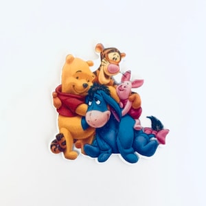 May include: A colorful sticker featuring Winnie the Pooh, Tigger, Piglet, and Eeyore. Winnie the Pooh is wearing a red shirt and hugging Tigger. Piglet is wearing a red dress. Eeyore is blue. The sticker is on a white background.