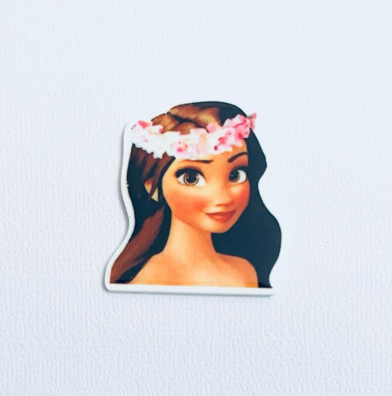 Op de afbeelding: Een sticker met een cartoonillustratie van een vrouw met bruin haar, bruine ogen en een roze bloemenkrans. De vrouw heeft een lichte huidskleur en een zachte glimlach. De sticker is uitgesneden rond de omtrek van de afbeelding.