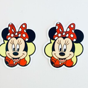May include: Two cartoon Minnie Mouse stickers with red polka dot bows and yellow backgrounds.