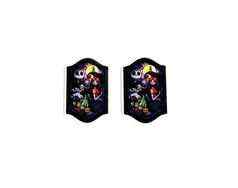 Może przedstawiać: Dwie pasujące ozdobne przypinki przedstawiające scenę z filmu "Miasteczko Halloween". Każda przypinka przedstawia Jacka Skellingtona, Sally i inne postacie na tle pełni księżyca i cmentarza. Przypinki mają czarną obw&oacute;dkę.