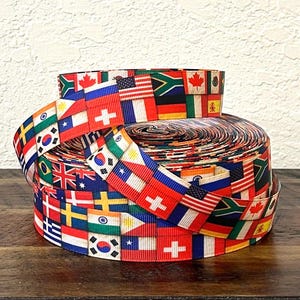 May include: A roll of ribbon featuring a repeating pattern of various national flags. The flags are displayed in a colorful and organized manner, with each flag clearly visible. The ribbon is likely used for crafting or decorative purposes.