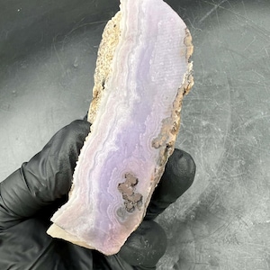 May include: A polished slab of purple agate with white and brown banding. The agate has a smooth, polished surface and is translucent.