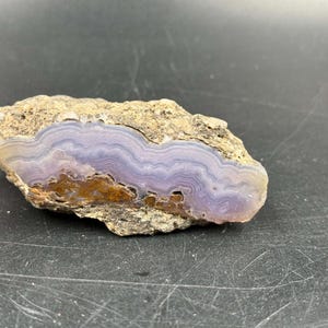 May include: A purple and brown agate geode with a rough exterior and a smooth, layered interior.