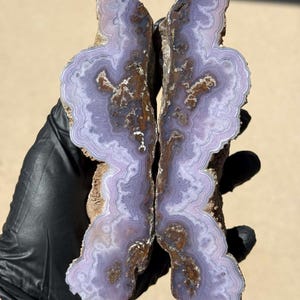 May include: Two halves of a purple agate geode with brown and white banding. The geode is cut and polished, revealing the intricate patterns inside.
