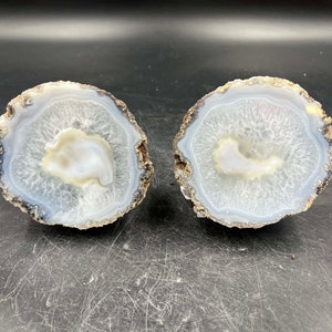 May include: Two agate slices with a white and gray banded pattern. The agate slices are polished and have a natural, organic shape.